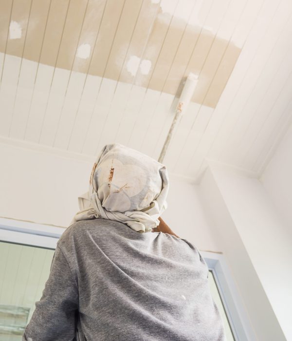 Partial focus photo of a man is painting ceiling using roller brush